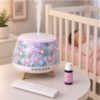 Floral-patterned humidifier on a white round table releasing mist, in a nursery with a sleeping baby in a crib nearby.