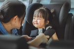 Image - Beanstalk Mums Young girl smiling while being buckled into a car seat by a caregiver in a car interior