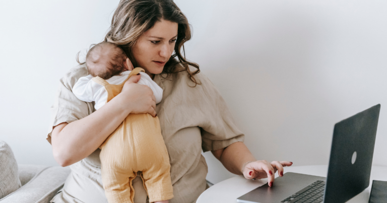 TPD cover - Beanstalk Mums Mother cradling a baby while using a laptop at a white table in a home setting. (informative image)